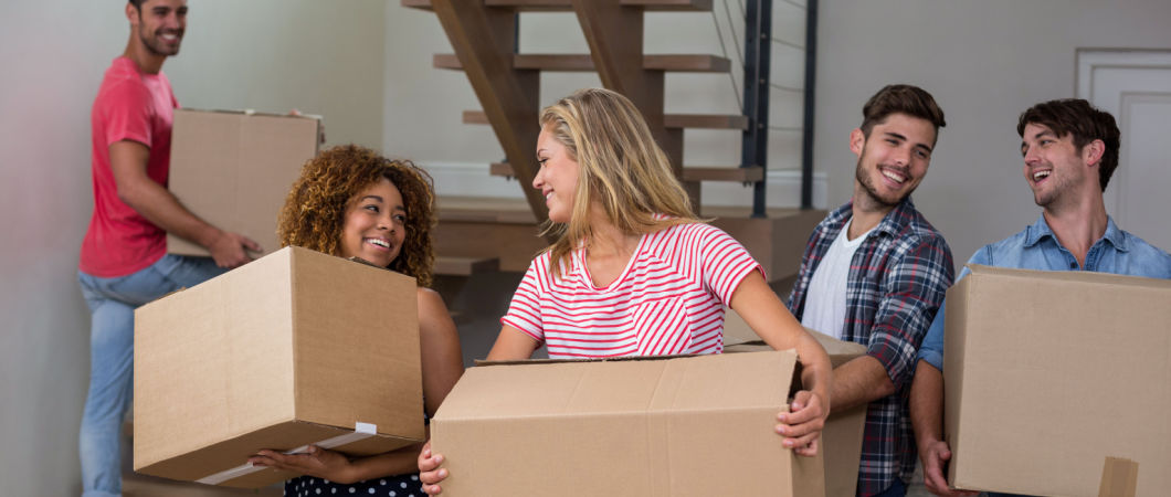 cheerful friends carrying cardboard boxes while relocating