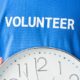 person holding wall clock in blue shirt with volunteer text